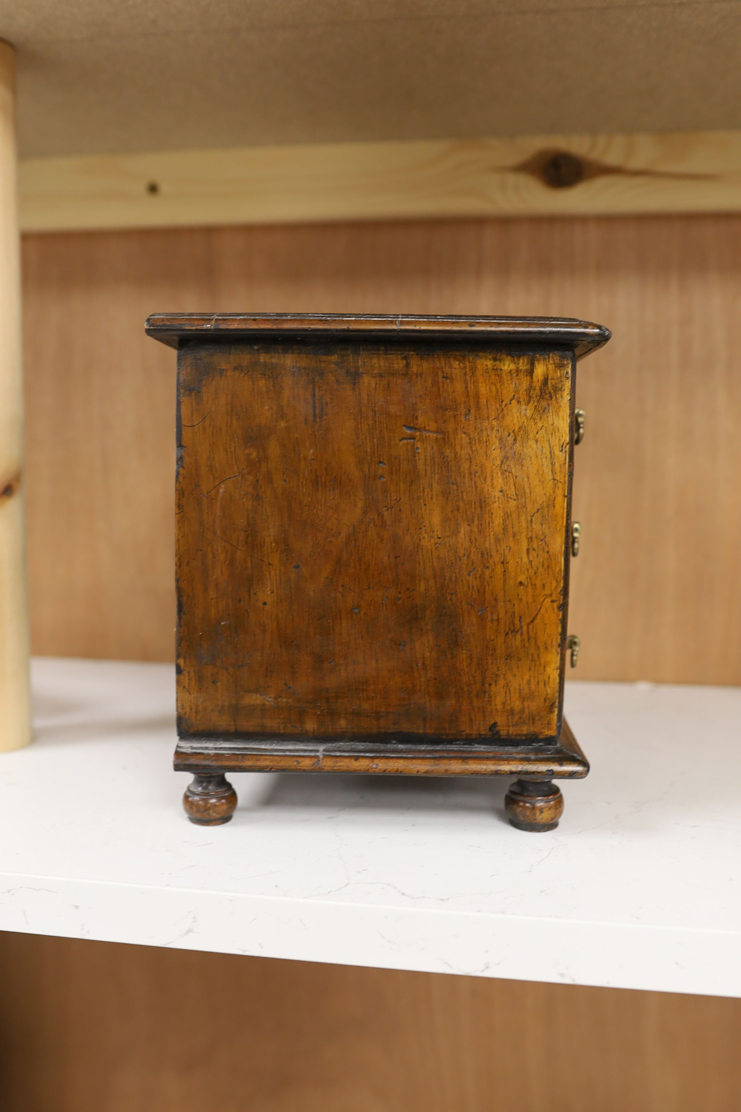 A cross banded walnut miniature chest of three drawers, 26cm wide